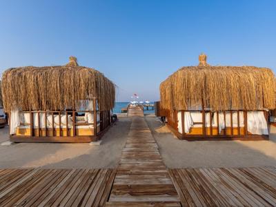 Holzsteg führt zu Strohhütten am Strand mit Blick auf das Meer und ein Boot.