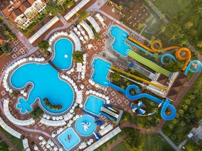 Vogelperspektive eines großen Hotelkomplexes mit verschiedenen Pools und Wasserrutschen in tropischer Umgebung.