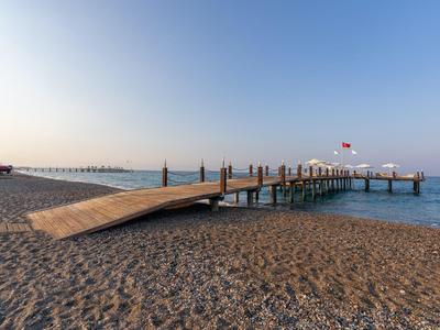 Langer Holzsteg erstreckt sich über felsigen Strand ins blaue Meer unter klarem Himmel.