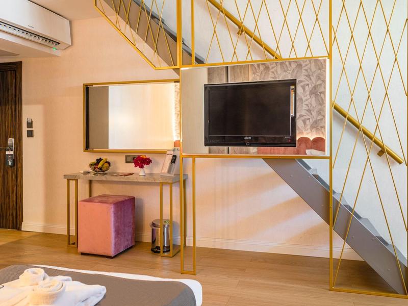 Area moderna della camera d'hotel con TV, scrivania, sgabello e corrimano giallo accanto alle scale.