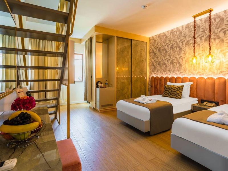 Camera d'hotel moderna con due letti, scala in legno e illuminazione calda.