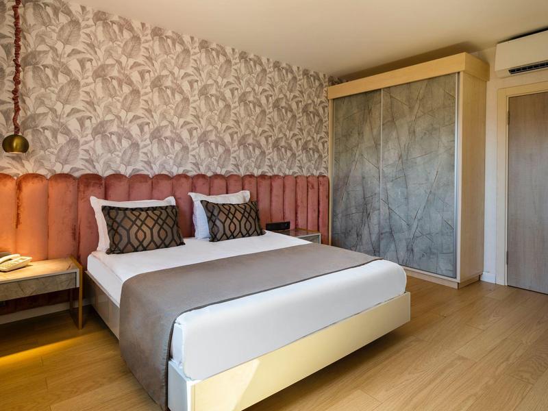 Camera d'hotel moderna con letto matrimoniale, cuscini decorati e porte scorrevoli effetto cemento.