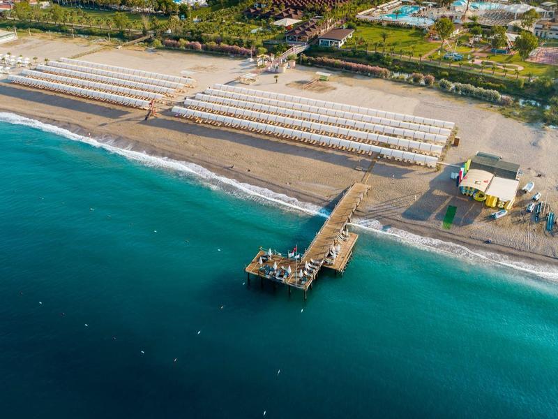 Vista aerea di una spiaggia con un molo che si estende nel mare blu e lettini sulla sabbia.