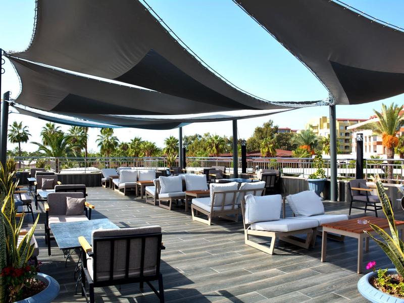 Terrazza esterna coperta con divani, tavoli e sedie, circondata da piante e tende da sole.