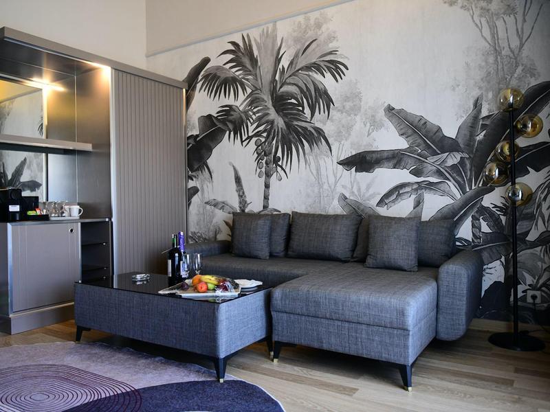 Camera d'hotel moderna con divano grigio e parete nera con motivi vegetali.