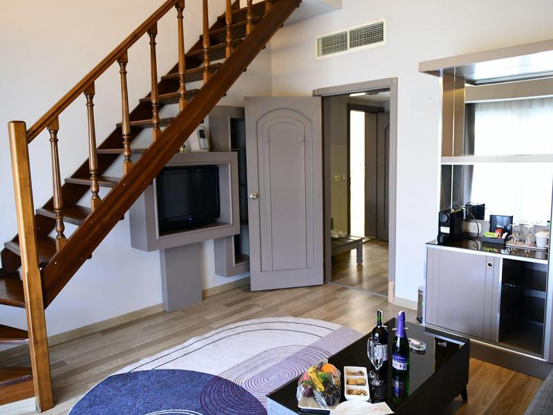 Camera d'albergo luminosa con scala in legno, TV a schermo piatto e angolo cottura moderno.