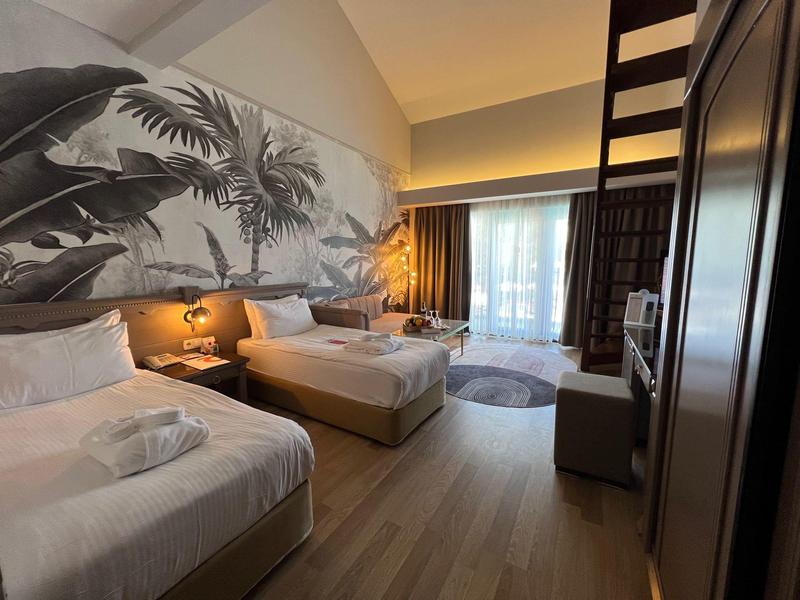 Camera d'albergo moderna con due letti, grande murale e grande finestra con tende.