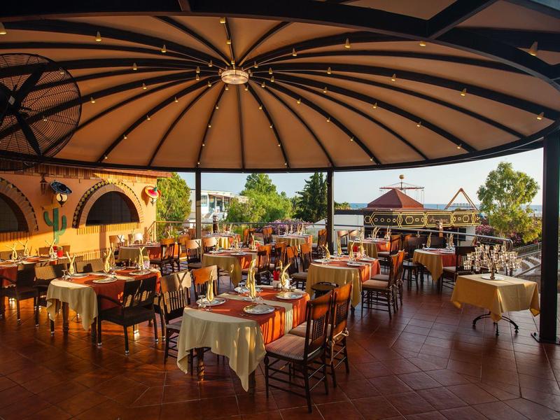 Grande terrazza coperta con tavoli apparecchiati e sedie in un ambiente soleggiato.