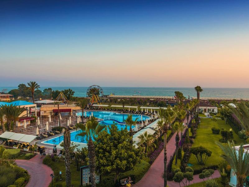Complesso alberghiero con più piscine, palme e vista mare al tramonto