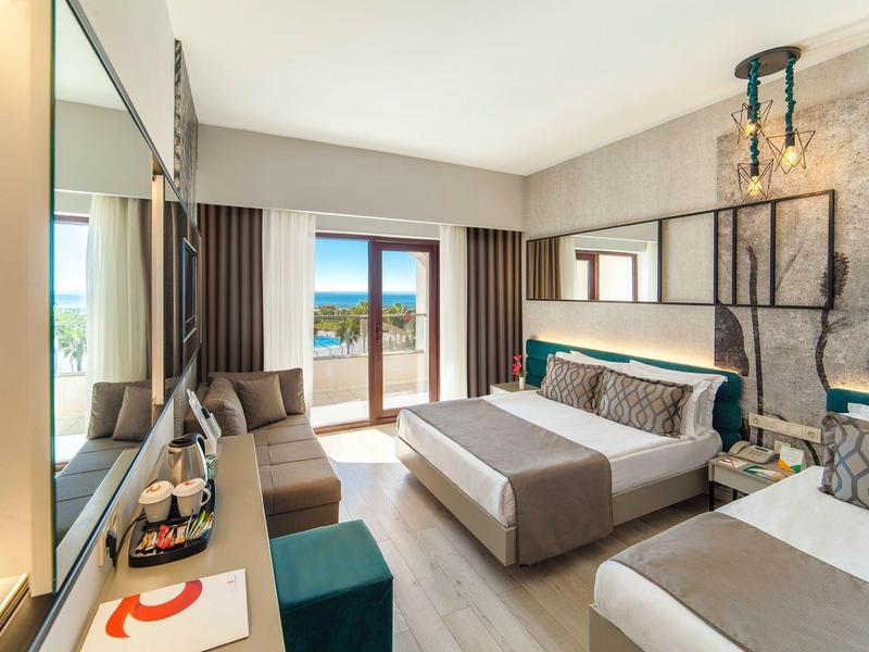 Camera d'hotel moderna con letto grande, divano e vista terrazza sul mare.