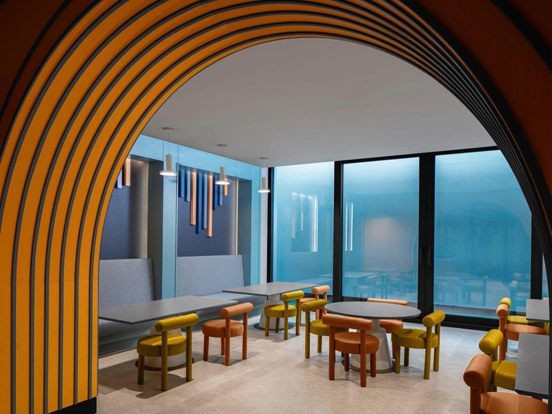 Área de salón moderna de hotel con muebles coloridos y ventana grande con vista.