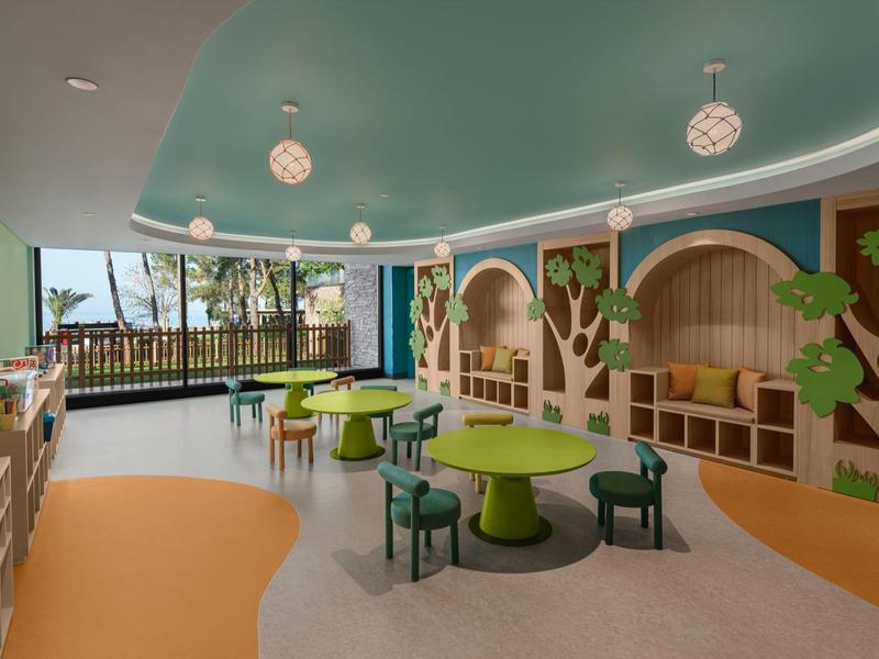 Sala de juegos infantil colorida con mesas, sillas, estanterías y decoraciones de árboles.