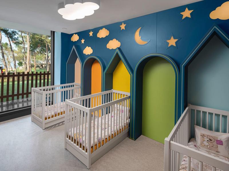 Sala de juegos infantil con camas, elementos de pared coloridos y decoración de estrellas y luna en la pared.