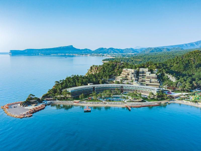 Resort de lujo en la costa con agua azul clara y colinas verdes al fondo.