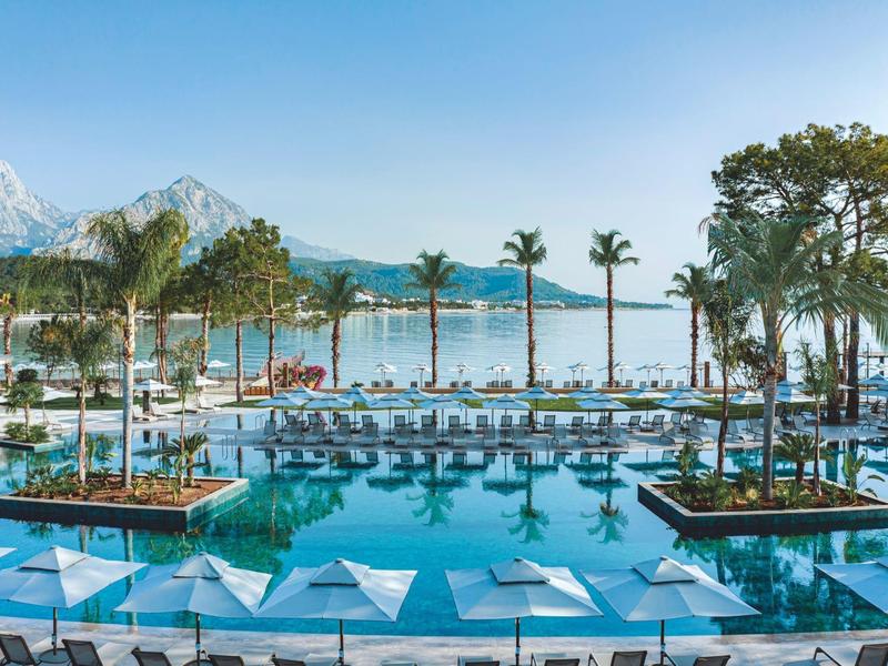 Área de piscina lujosa con palmeras y vista a montañas y lago bajo cielo despejado.