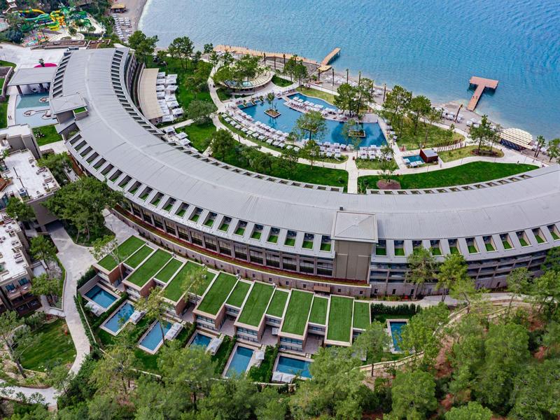 Vista aérea de un complejo hotelero con piscina, acceso a la playa y jardines en la azotea junto al mar.