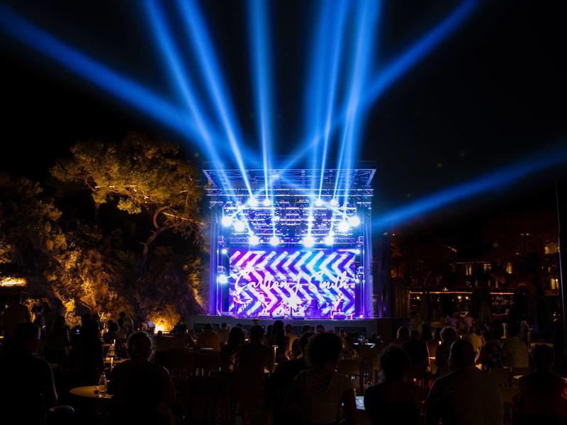 Rayos azules brillantes irradian de un escenario en un evento nocturno al aire libre.