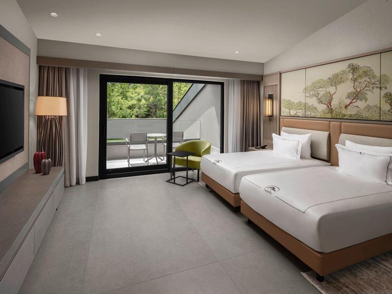 Moderna habitación de hotel con dos camas individuales, TV, área de descanso y terraza con vista a la naturaleza.