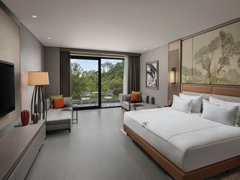 Habitación de hotel moderna con cama doble, área de estar y ventana grande con vista al verde.