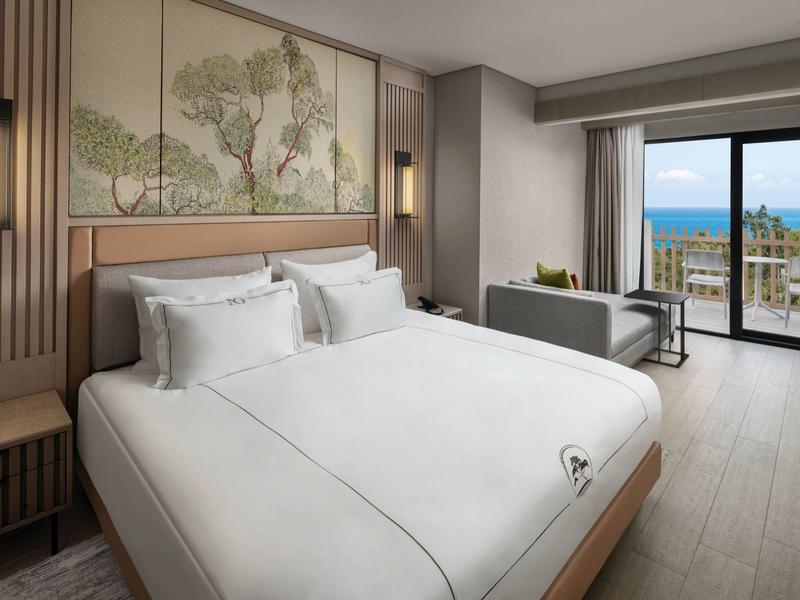 Habitación de hotel moderna con cama doble y vista al mar a través de grandes ventanas de balcón.