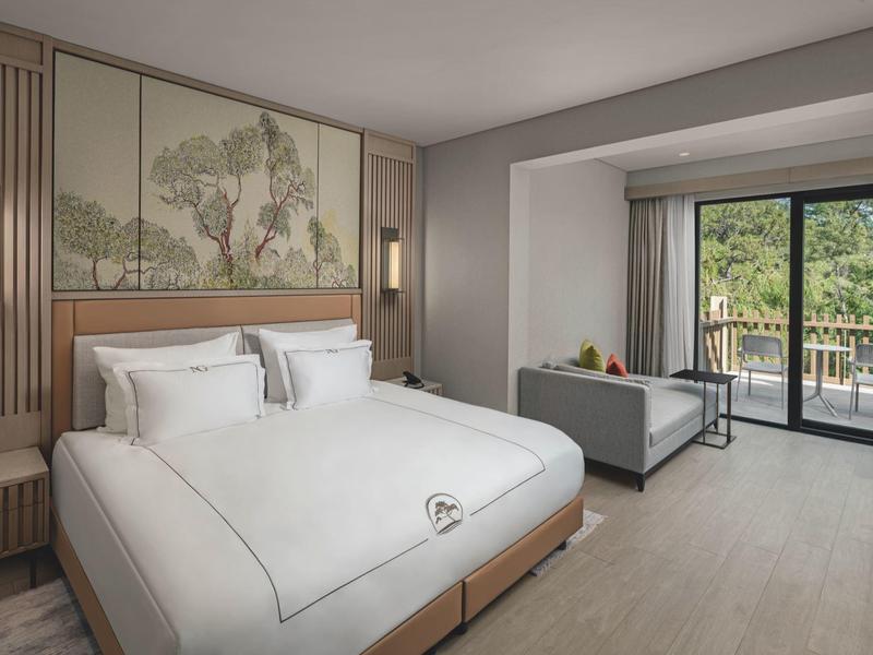 Habitación de hotel luminosa con cama grande, arte natural en la pared y balcón con vistas.