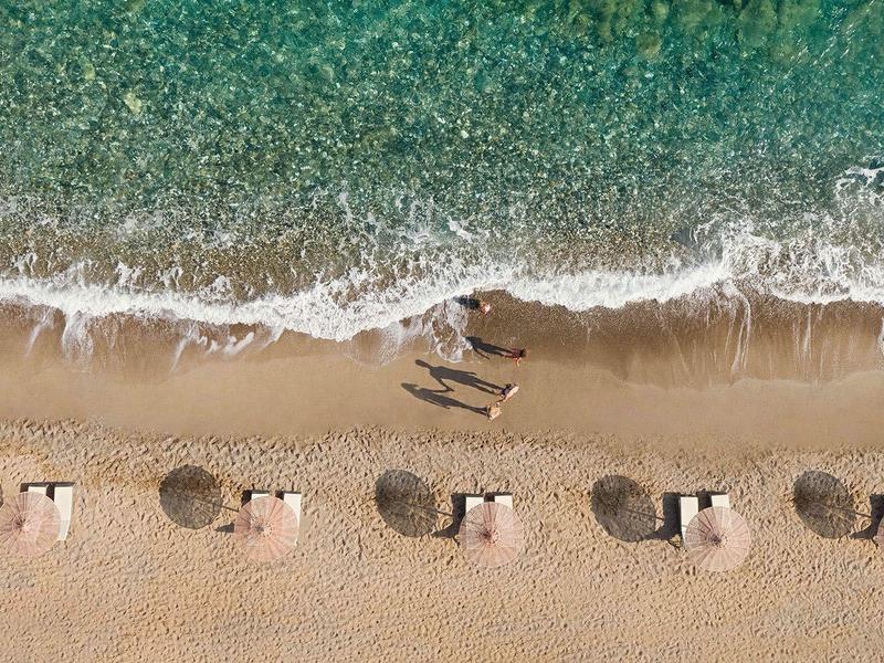 Vista aérea de una playa con tumbonas y sombrillas dispuestas en parejas junto al agua.