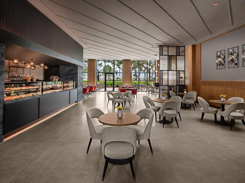 Área elegante de salón de hotel con sillas modernas, mesas y gran ventana con vista al jardín.