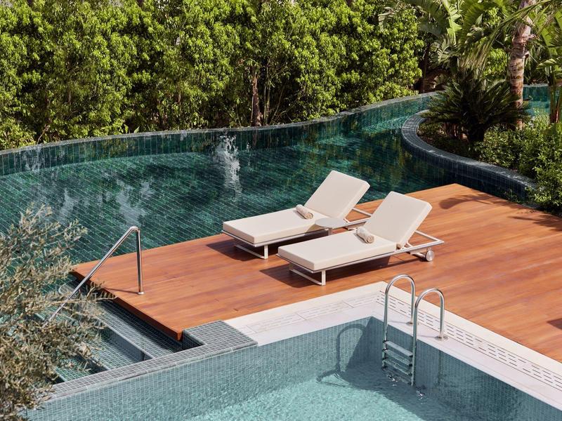 Area piscina con due lettini su solarium in legno circondato dal verde.