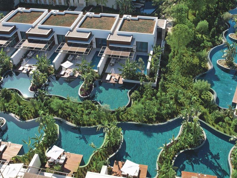 Vista aerea di un resort con piscine collegate e ville moderne in ambiente tropicale.