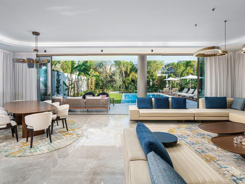 Ampio soggiorno con grandi finestre, mobili moderni e vista su giardino e piscina