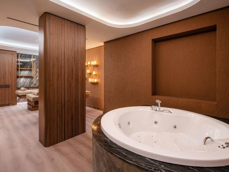 Vasca idromassaggio moderna in una camera d'hotel di lusso con illuminazione indiretta ed elementi in legno.