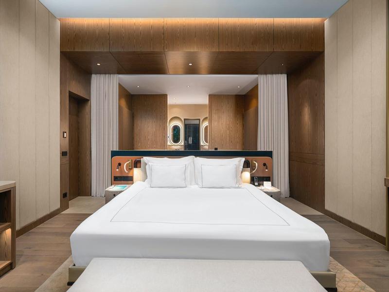 Camera d'hotel moderna con un grande letto, pareti in legno e illuminazione indiretta.