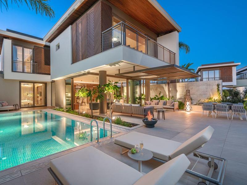 Villa moderna con piscina illuminata, lettini e area esterna al tramonto.