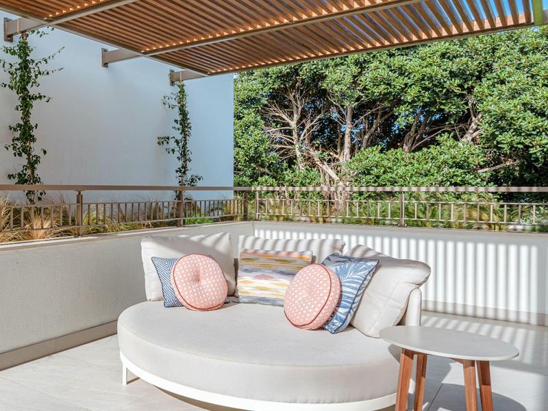 Area esterna moderna con divano rotondo, cuscini e pergolato in legno su terrazza con vista sugli alberi.