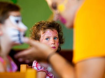 Child with face paint looks attentively in a colorful indoor setting.