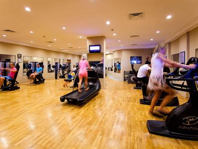 Gimnasio con suelo de madera y varias personas en cintas de correr y usando pesas.