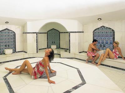 Three people relax in a bright, Arabesque-style spa with tiled benches.