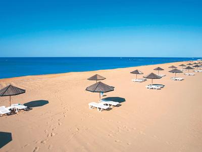 Empty sandy beach with sun loungers and parasols under clear blue sky