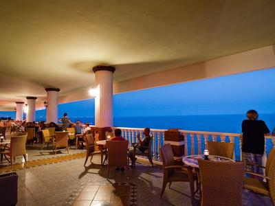 Evening hotel terrace with tables, chairs, and a view of the blue sea.
