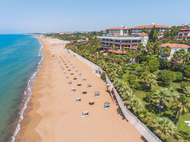 Long sandy beach with sun umbrellas and adjacent hotels under a blue sky.