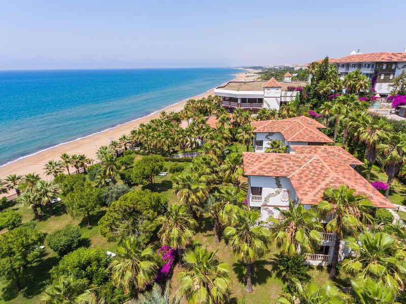 View of tropical beach with hotel and palm trees under a blue sky.