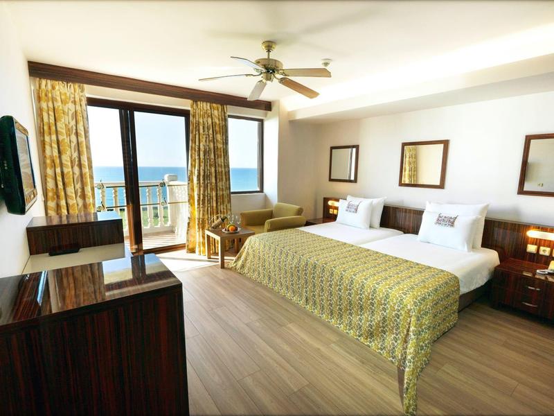 Bright hotel room with two single beds and balcony overlooking the sea.