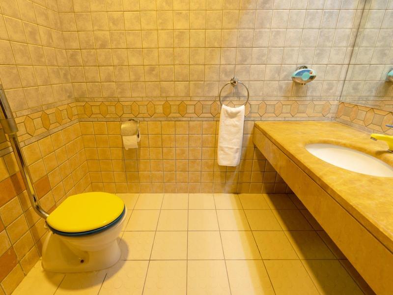Bright bathroom with yellow-tinted toilet seat and large mirror above the sink.