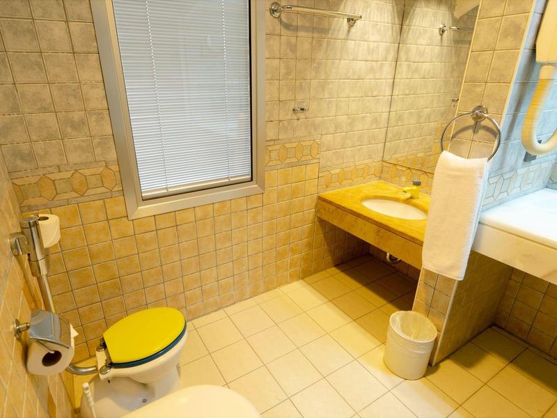 Bright bathroom with yellow toilet seat, sink, towel holder, and hairdryer next to a bathtub.