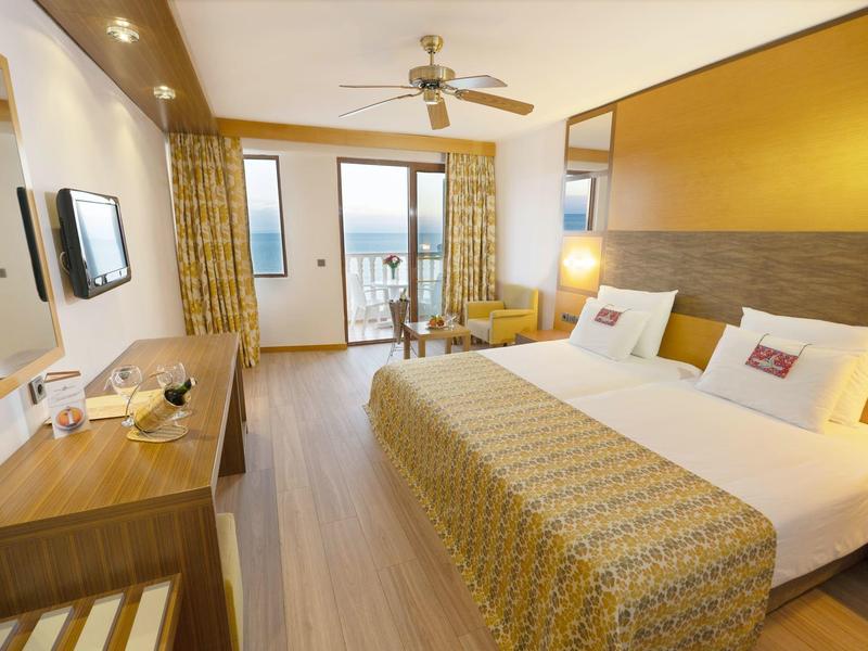 Bright hotel room with double bed, desk, balcony, and sea view.