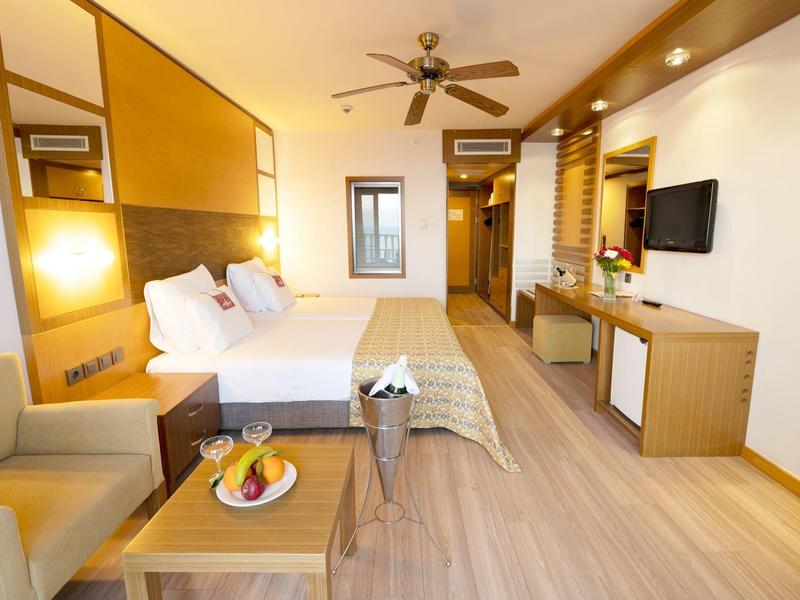 Bright hotel room with large bed, ceiling fan, and cozy seating area.