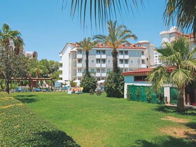 Edificio dell'hotel con balconi, prato verde, palme e cielo azzurro soleggiato