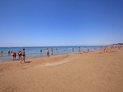 Spiaggia di sabbia con persone che camminano e nuotano sotto un cielo azzurro.