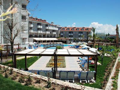 Area piscina con lettini, ombrelloni e un grande edificio dell'hotel sullo sfondo in una giornata di sole.