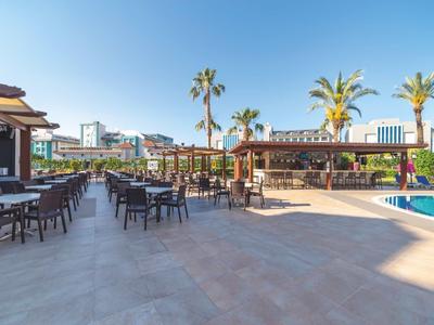 Ampio patio esterno dell'hotel con tavoli, sedie, palme e cielo azzurro.